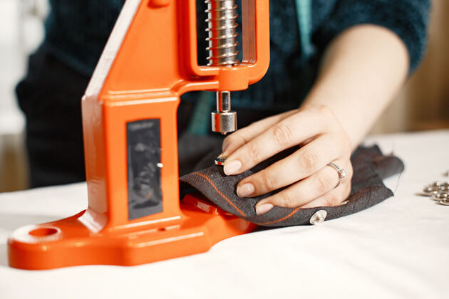 专业橙色熨烫衣服织物上的纽扣带着缝纫工具的女人工艺衣服人
