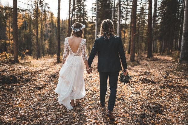 人类白天 新娘和新郎在树林里的落叶地上散步金发夫妇衣服