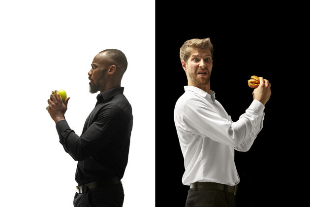 三明治在黑白背景下吃汉堡包和新鲜水果的男人快乐的非洲和高加索男人汉堡包 快餐 健康和不健康的食物概念夫妇水果健康