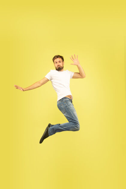 帅气黄色背景上孤立的快乐跳跃人的全长肖像穿着休闲服的白人男模自由选择 灵感 人类情感概念给予五 问候 自信人类牛仔裤办公室