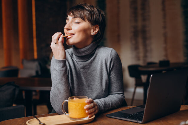 坐着年轻的女人在电脑前工作 喝着热茶学习年轻餐厅