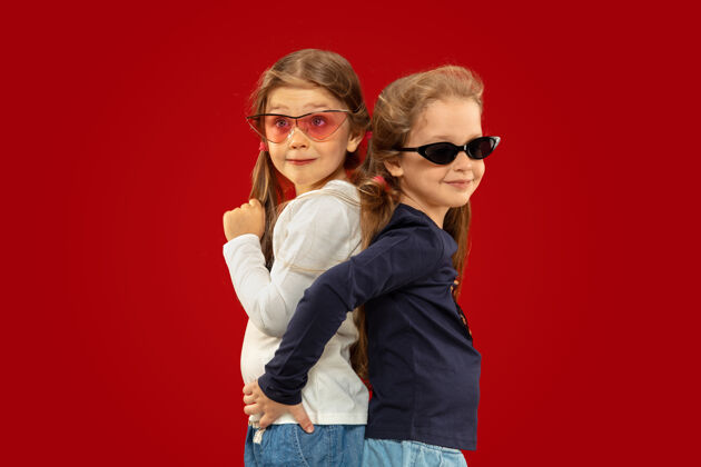 情绪美丽动情的小女孩被隔离在红色背景上戴着红黑墨镜的快乐姐妹或朋友的半幅肖像面部表情的概念 人类的情感 童年童年金发头发
