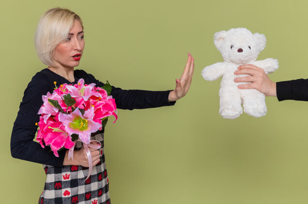 手势拿着一束鲜花的年轻女子在接受泰迪熊作为礼物时做了一个停下来的手势衣服绿色停止