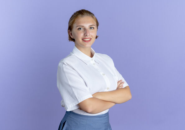 金发年轻的微笑的金发俄罗斯女孩交叉双臂站在紫色背景上与复制空间隔离微笑交叉站着