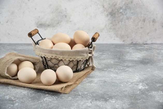堆篮子和麻布有机新鲜生鸡蛋放在大理石表面鸡早餐烹饪