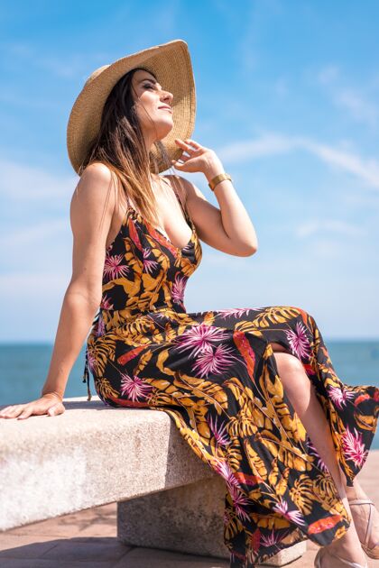 垂直在西班牙拍摄的一个女性穿着花太阳裙 戴着帽子坐在海边的垂直镜头海岸天空海