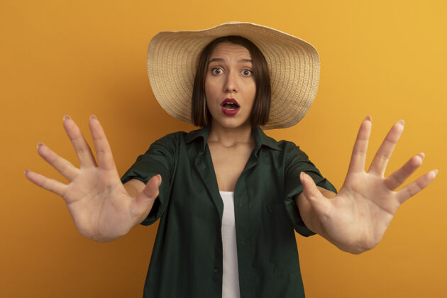 焦虑焦急的漂亮女人 戴着沙滩帽 伸出双手 孤零零地站在橙色的墙上帽子人手