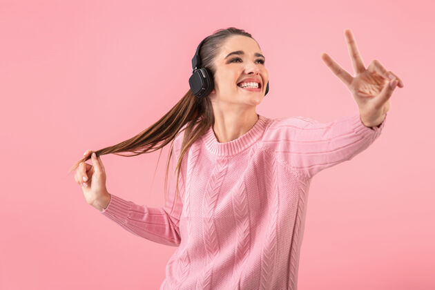 无线年轻漂亮的女人戴着无线耳机听音乐 穿着粉色毛衣微笑着立体声欢呼女士