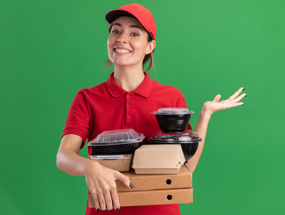 人身着制服的年轻漂亮的送货员微笑着 拿着比萨饼盒上的纸质食品包装和容器 在绿色的墙上保持手的张开与隔离表情感觉站立