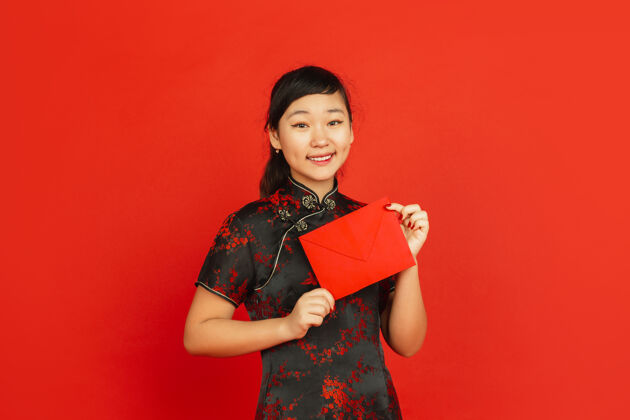 手2020中国新年红色背景上孤立的亚洲少女肖像身着传统服装的女模特看起来很开心 微笑着拿着红包庆祝 节日 情感中国女孩美丽