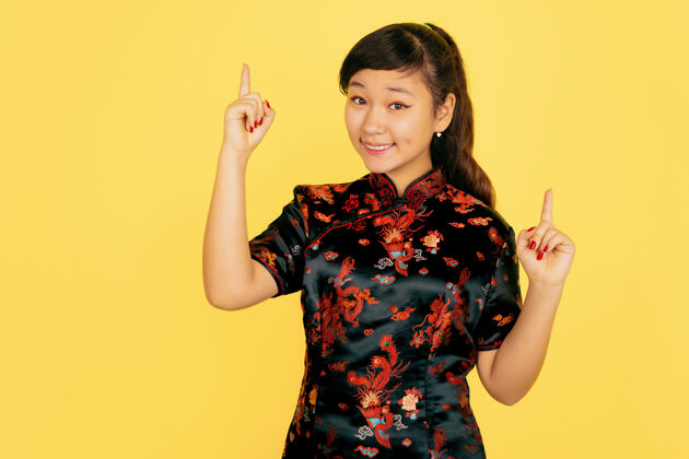 女孩可爱的微笑 指向上2020年中国新年快乐黄色背景上的亚洲少女肖像穿着传统服装的女模特看起来很快乐庆祝 人类情感复制空间普通话服装旗袍