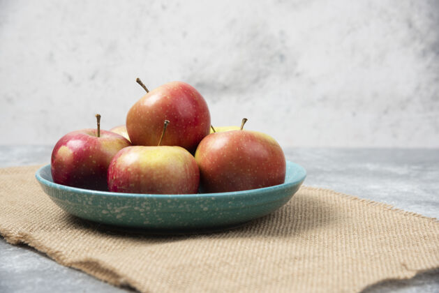 红色在大理石上放满新鲜苹果的蓝色碗生的成熟桌布