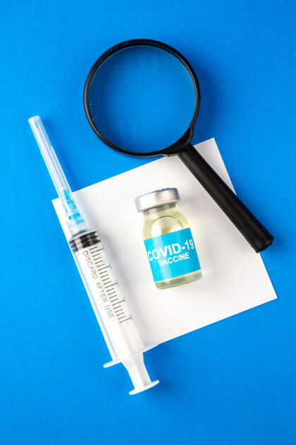 放大镜俯视图带放大镜的疫苗和蓝色表面的注射医院健康疫苗-实验室科学大流行病毒药物视图医院药品