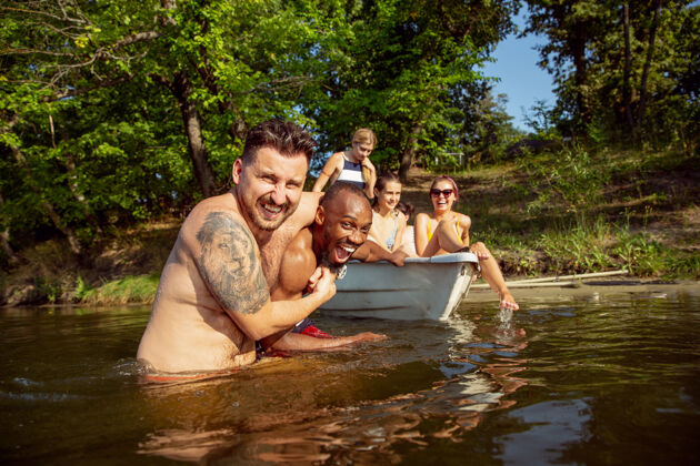 欢呼一群快乐的朋友在河里欢笑和游泳阳光明媚的日子里 穿着泳装的男女们在河边乘船欢庆夏日 友谊 度假 周末的概念朋友友谊游泳