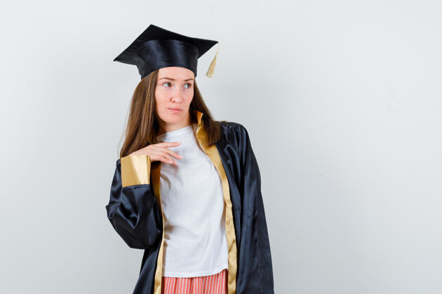 年轻女毕业生摆着姿势 穿着学院服 目光集中前视图欢呼Cap长袍