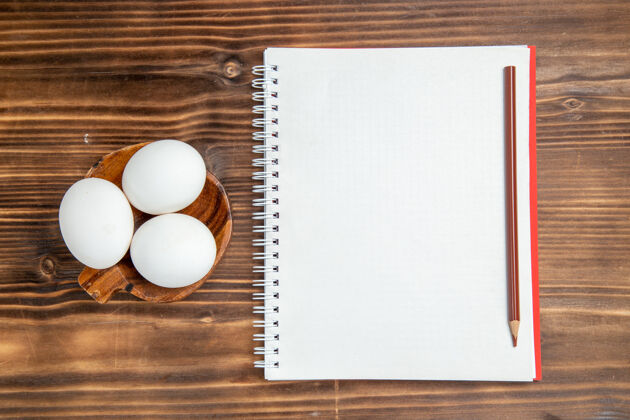 信息俯视整个生鸡蛋与记事本上棕色的木制表面餐食品早餐木顶部生的空白