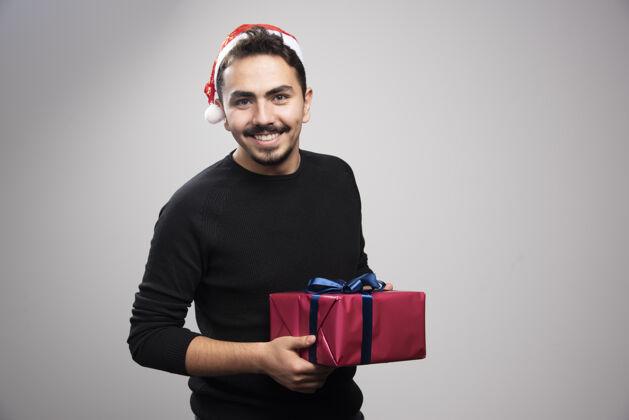 礼物一个年轻人拿着一个礼品盒在灰色的墙上帽子礼物姿势