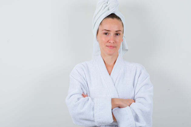 头发年轻的女士交叉双臂站在白色浴衣 毛巾和看起来自信前视图毛巾成人漂亮