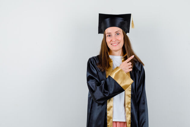 女人年轻的女毕业生穿着学院服指着右上角 看上去很高兴正视图时尚新鲜头发
