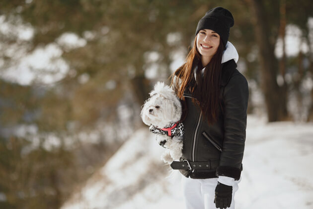 一个在冬季公园散步的可爱女孩穿着棕色夹克的女人牵着狗的女人女孩聚在一起散步
