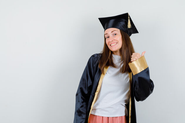 大学女毕业生穿着学院服 露出大拇指 看起来很开心正面图微笑帽子学校