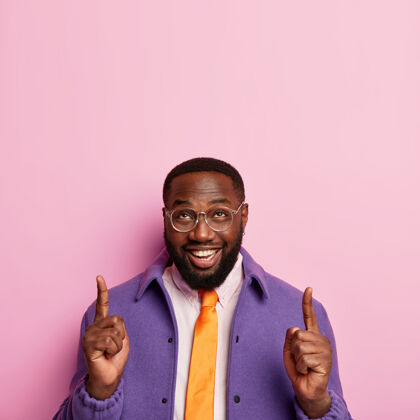 表情开朗的没刮胡子的男人竖起食指 展示成功的想法 推广复制空间 戴眼镜 橙色领带和紫色外套展示男性手