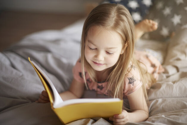 羽绒被小女孩在床上看书的特写照片婴儿微笑就寝时间