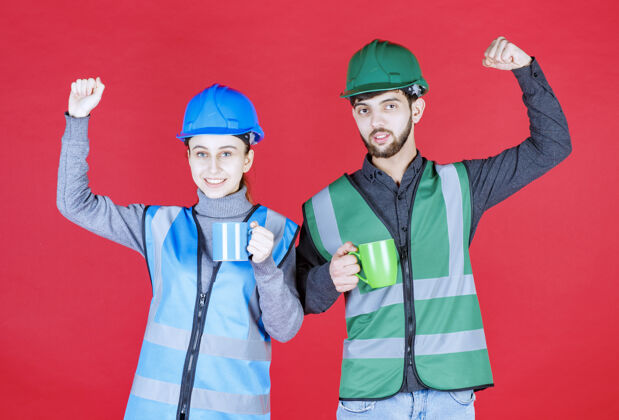咖啡男女工程师戴头盔 手持蓝绿色马克杯 并显示满意标志人满意装备