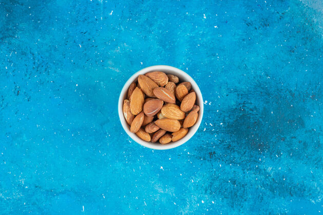 健康在蓝色表面的碗里放着没有壳的杏仁杏仁美味美味
