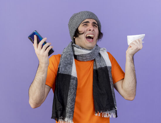 餐巾愤怒的年轻病人戴着冬天的帽子 戴着围巾 拿着电话 用餐巾隔离在紫色的背景上愤怒帽子电话