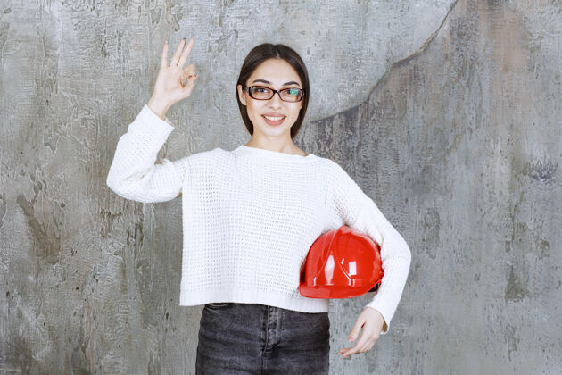 墙女工程师戴着红色头盔 手上有积极的手势成年人工程师建筑