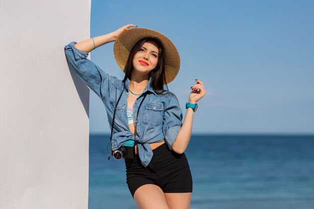 欢乐穿着短裤戴着草帽在沙滩上摆姿势的快乐女人乐趣水优雅