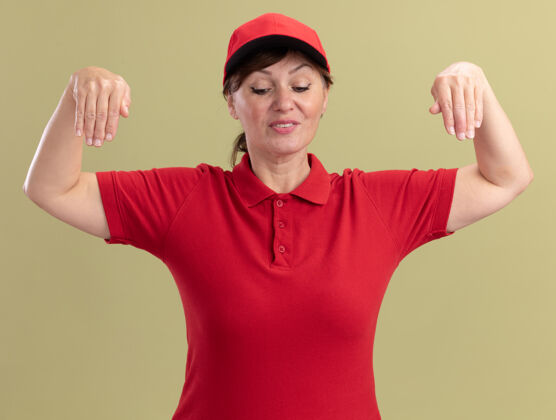 立场身穿红色制服 头戴鸭舌帽的中年女送货员站在绿色的墙上 双手自信地打着手势帽子年龄女人