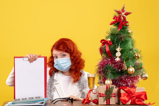 年份前视图女医生围绕圣诞树和礼物坐在面具到处节日花束