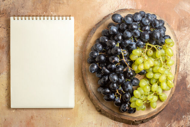 有机顶视图葡萄木板与绿色和黑色葡萄旁边的白色笔记本可食用的水果葡萄纸板
