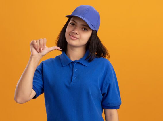 递送身穿蓝色制服 头戴鸭舌帽的年轻送货员站在橙色的墙上 自信地微笑着看着自己帽子年轻站立