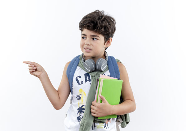 小学生看着身边高兴的小男生背着书包 戴着耳机拿着书 指着旁边隔离的白色背景和复印空间点请穿小的