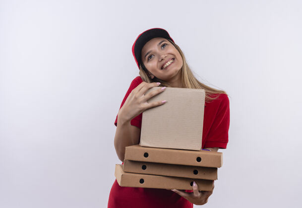 帽子看着快乐的年轻送货女孩穿着红色制服 戴着帽子 拿着盒子隔离在白色背景上 留着复印空间盒子喜悦交货
