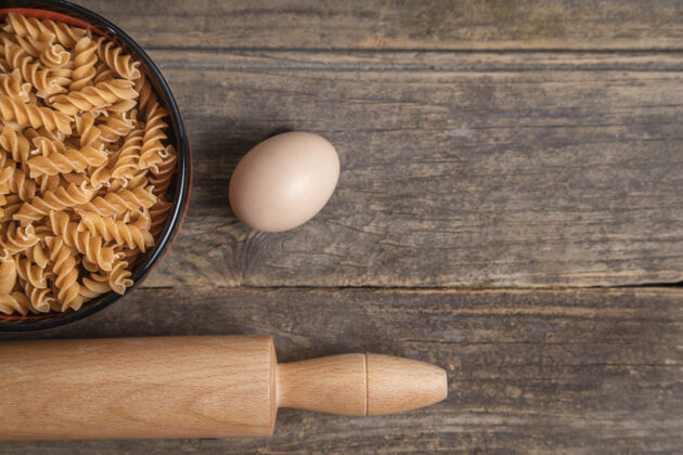 生的一碗生的干意大利面 擀面杖和鸡蛋在木制背景上高品质的照片烹饪生的鸡肉