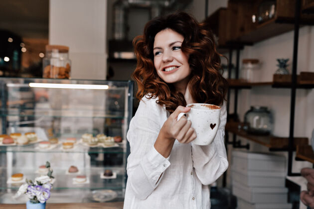 肖像微笑的年轻女士拿着一杯咖啡站在柜台前等待顾客的画像美丽咖啡商务