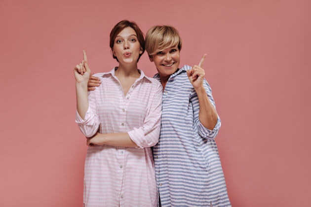 女儿漂亮的两位女士 时尚短发 夏季条纹连衣裙 拥抱并展示给粉色背景上的文字短发粉色背景衬衫
