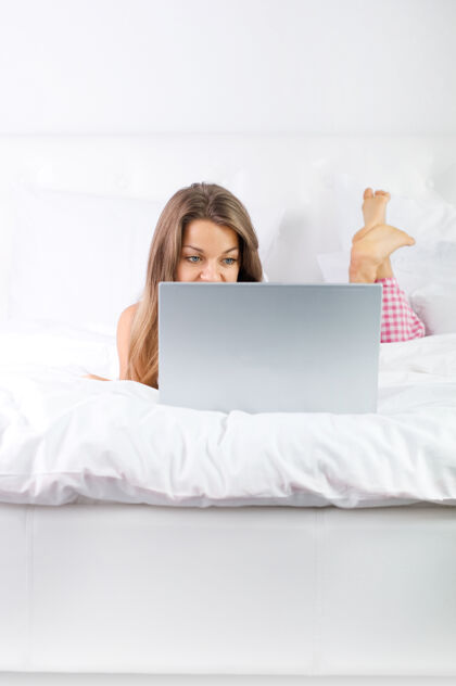 可爱年轻女子在床上使用笔记本电脑床棕色头发年轻人