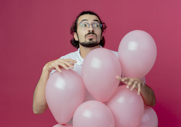穿看着一旁想着戴眼镜的帅哥站在粉色背景上孤立的气球后面壁板眼镜思考