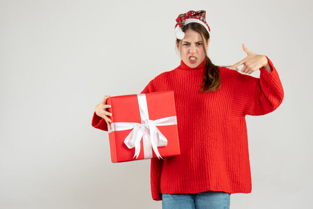工作前视图愤怒的女孩拿着圣诞帽拿着礼物指着自己手手指帽子