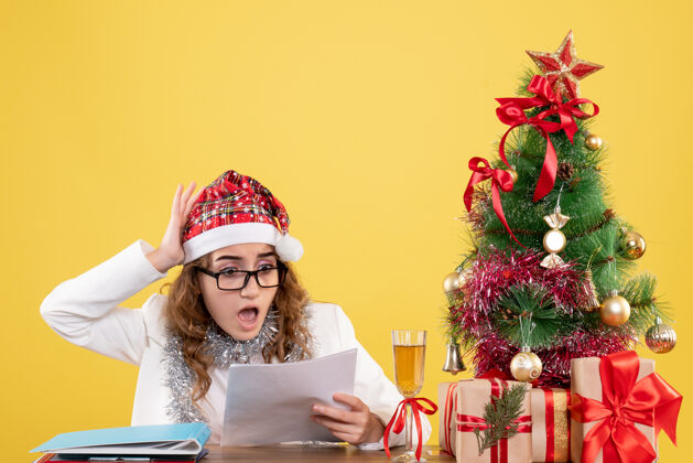 圣诞树前视图女医生在她的桌子后面拿着文件餐桌节日文件