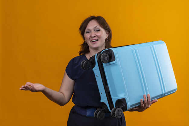 中年人高兴的中年旅女拿着手提箱 用手指着孤立的橙色背景壁板手点