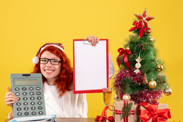 花前视图女医生拿着计算器围着圣诞礼物和圣诞树年礼物房子