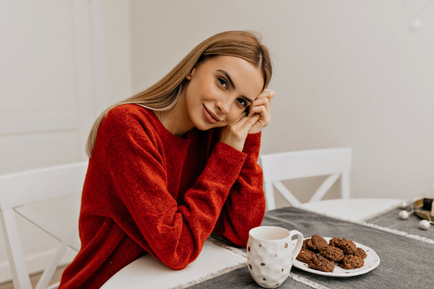 灵感穿着红毛衣的可爱可爱女孩早上坐在厨房里喝着咖啡和饼干和平房间生活