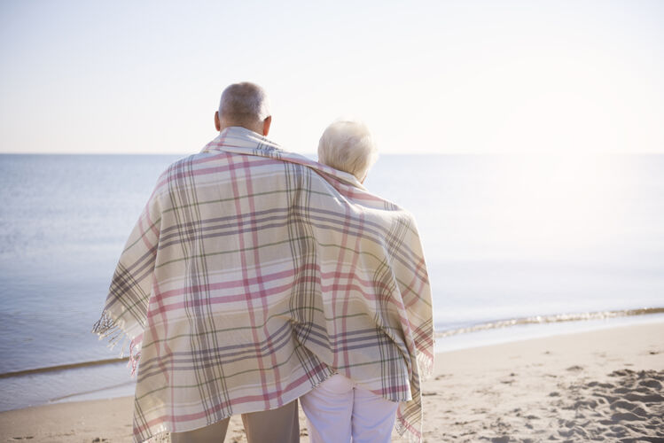 祖父老人们站在沙滩上 身上裹着温暖的毯子约会享受浪漫