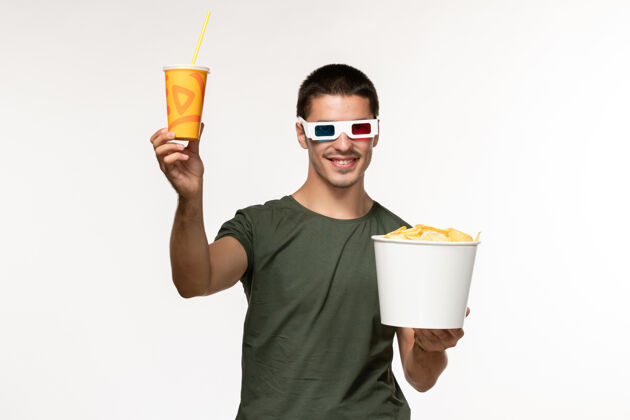电影正面图身穿绿色t恤的年轻男性手持土豆cips苏打水in-d太阳镜在白色墙上拍摄电影男性孤独电影电影院职业电影年轻的男人